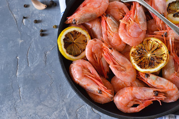 Boiled shrimps with lemon in a frying pan on a concrete background