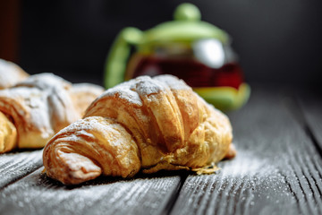 croissants with tea on dark wooden background close-up