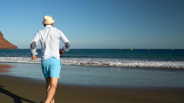Happy man runs to the ocean beach at sunset. Concept of carefree modern life. Tenerife, Canarian Islands. Slow motion
