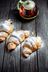 three croissants with tea on dark wooden background close-up top view