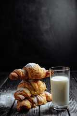 three croissants with glass of milk on dark wooden background close-up
