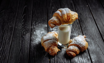 three croissants with glass of milk on dark wooden background close-up top view