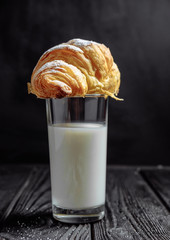 croissant on glass of milk on dark wooden background close-up