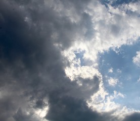 Obraz premium The sun though the gray and white clouds in the sky.