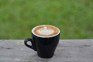 A cup of latte art coffee above old wood plate on blur green field background
