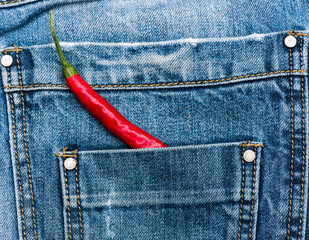 Pepper in back pocket of blue jeans. Pocket of jeans staffed with red chilly pepper, denim background. Piquant secret in pocket of pants, top view. Hot sensations concept