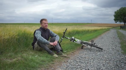 The guy is sitting on the grass near the bike on the background of the field. Adaptation to virus COVID 19 self-isolation 