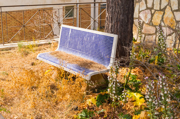 Rounded bench made of small square blue mosaic give up under a tree