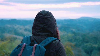 backpack and camping concept from woman in warm cloth with her bag travel and see to forest and mountain in morning after sunrise
