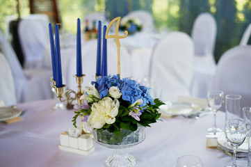 Table with a classic design. With a composition in a high vase with hydrangeas and lilies, a Golden candlestick with blue candles. Decor and floristry
