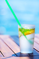 Mojito cocktail with lime and mint in highball glass on wooden table near pool.