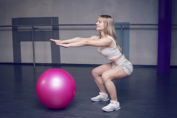 Fit young pretty woman doing squats exercises with fitness ball. side view.