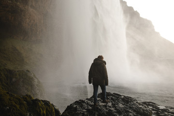 Man wearing a coat under a waterfall in iceland in winter - Powered by Adobe