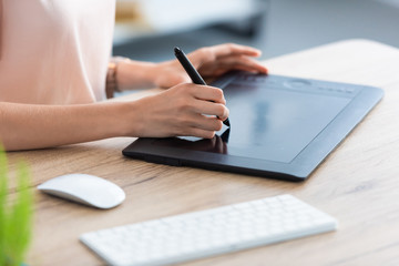 cropped image of female freelancer drawing on graphic tablet at table in home office