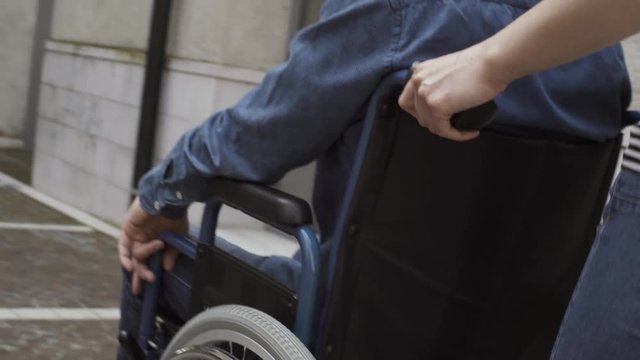 Woman pushing a man in wheelchair in the city street