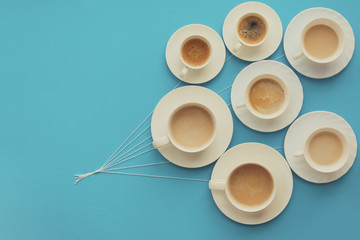 Hand holding coffee cups with milk and without in shape of balloons on blue paper background. Weather concept. Food art. Coffee splash. Flat Lay. Top view. Copy space. Toned