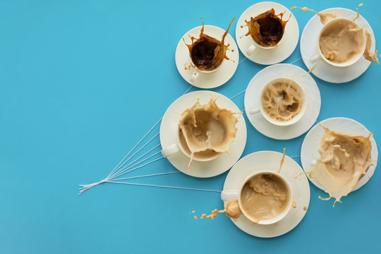 Hand holding coffee cups with milk and without in shape of balloons on blue paper background. Weather concept. Food art. Coffee splash. Flat Lay. Top view. Copy space. 