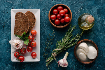 Mozzarella cheese and tomatoes on dark blue table with bread and herbs