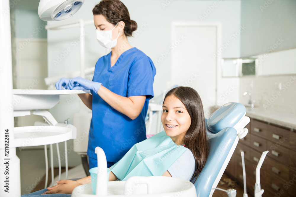 Wall mural Smiling Girl Sitting On Chair While Dentist Working In Clinic