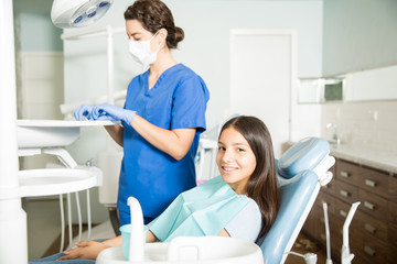 Smiling Girl Sitting On Chair While Dentist Working In Clinic