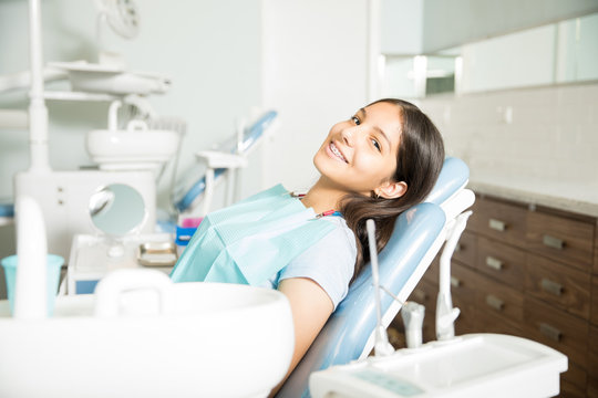 Portrait Of Smiling Girl With Braces Sitting At Clinic