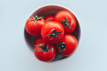 Red tomatoes in a white bowl on white background