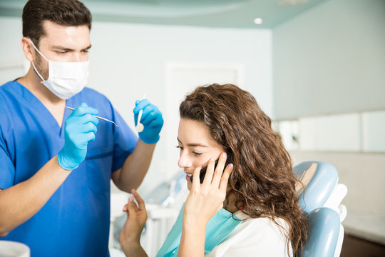 Dentist Standing By Female Patient Using Mobile Phone In Clinic