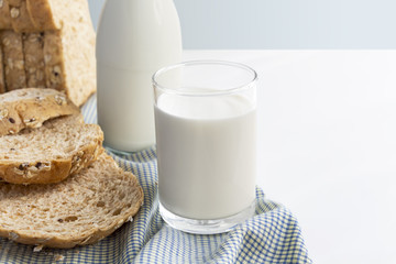A bottle of milk and glass of milk with sliced bread on cloth isolated on white table with gray background for food and healthy concept. with copy space for text.