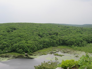 View over the edge of a cliff on a mountain on Lantern Hill trail in Connecticut, with a pond below in the distance 