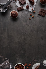 Baking background with chocolate muffins, measuring cups, chocolate, sugar and nuts on dark concrete background. Flat lay with copy space in the middle.