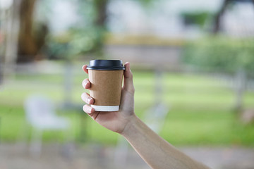 Disposable White Coffee Cup with Black Lid holding on hand for takeaway on a blur green Background