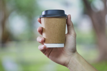 Close up of Disposable White Coffee paper Cup with Black Lid holding on hand for takeaway on blur green Background
