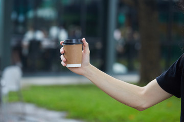 Disposable plastic White Coffee Cup with Black Lid holding on hand for takeaway on a blur green Background