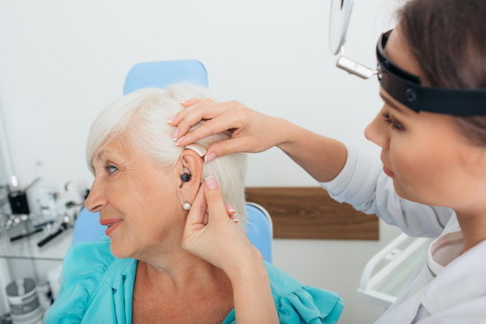 doctor helping elderly woman inserting hearing aid