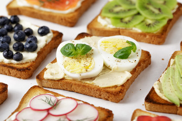 Sandwich with eggs and hummus with different toasts on white table.