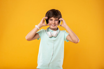 I love technology. Joyful handsome boy holding two phones and wearing headphones