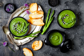 Homemade green spring asparagus cream soup decorated with black sesame seeds and edible chives flowers