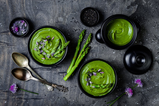 Homemade green spring asparagus cream soup decorated with black sesame seeds and edible chives flowers