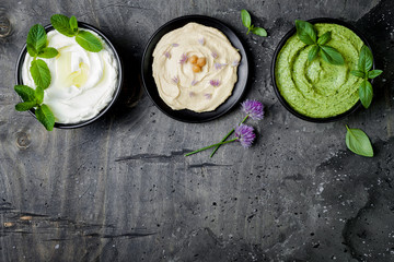 Vegetarian dip table. Yogurt sauce or labneh, hummus, herb hummus or pesto. Middle eastern meze snacks set. Copy space, flat lay, overhead