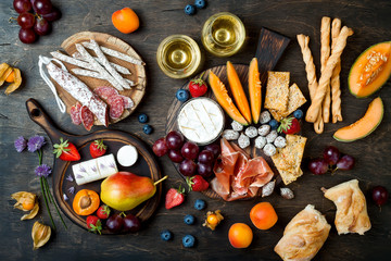 Appetizers table with italian antipasti snacks and wine in glasses. Cheese and charcuterie variety board over rustic wooden background