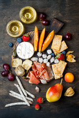 Appetizers table with italian antipasti snacks and wine in glasses. Cheese and charcuterie variety board over rustic wooden background