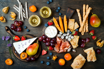 Appetizers table with italian antipasti snacks and wine in glasses. Cheese and charcuterie variety board over rustic wooden background