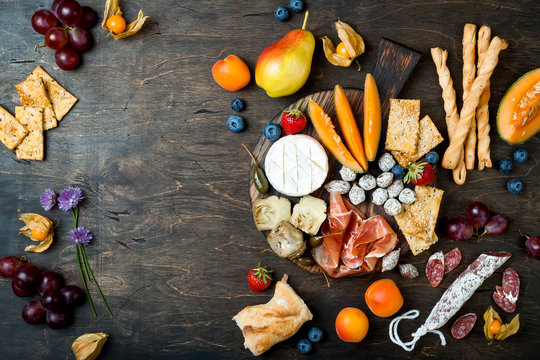Appetizers table with italian antipasti snacks. Cheese and charcuterie variety board over rustic wooden background