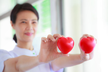 Red heart held by smiling female nurse's hand, representing giving effort high quality service mind to patient. Professional, Specialist in white uniform concept