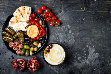 Fototapeta na wymiar Arabic traditional cuisine. Middle Eastern meze platter with pita, olives, hummus, stuffed dolma, labneh cheese balls in spices. Mediterranean appetizer party idea
