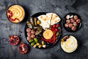 Arabic traditional cuisine. Middle Eastern meze platter with pita, olives, hummus, stuffed dolma, labneh cheese balls in spices. Mediterranean appetizer party idea - obrazy, fototapety, plakaty
