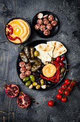 Fototapeta na wymiar Arabic traditional cuisine. Middle Eastern meze platter with pita, olives, hummus, stuffed dolma, labneh cheese balls in spices. Mediterranean appetizer party idea