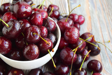 Sweet cherry fresh ripened is in a white cup and near a cup. Drops of water are on sweet cherry.