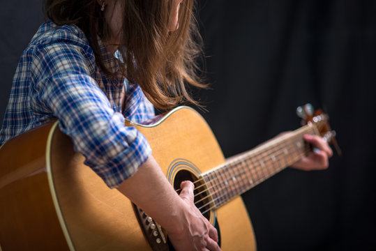 Girl teenager playing an acoustic guitar on a dark background in the Studio. Concert young musicians