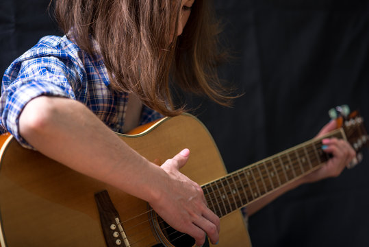 Girl teenager playing an acoustic guitar on a dark background in the Studio. Concert young musicians